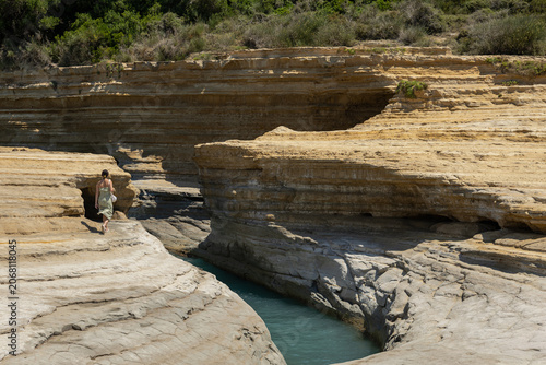 woman walking along narrow turquoise sea channel between unique sandstone rock formations in sidari corfu greece