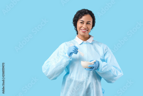 Happy young African-American female scientist with mortar and pestle on blue ...