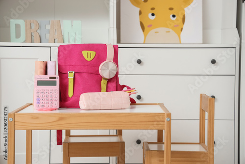 Pink backpack with headphones and stationery on table in childrens room