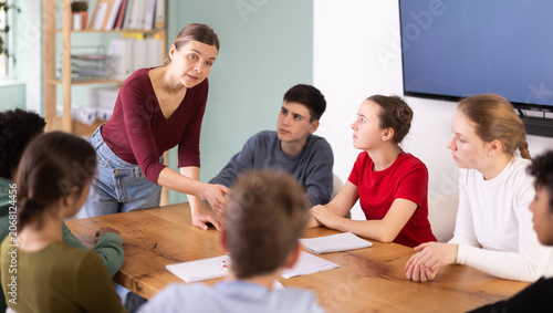 Cuadro en lienzo Active female teacher speaking to attentive teenage students sitting around tabl