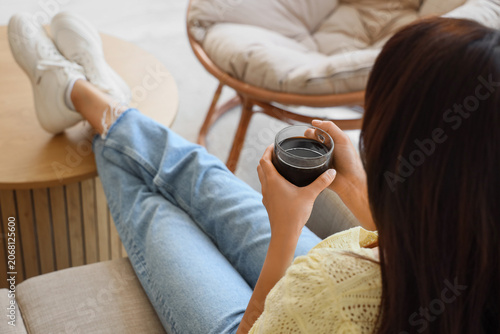 Young woman with cup of coffee sitting on sofa at home, closeup