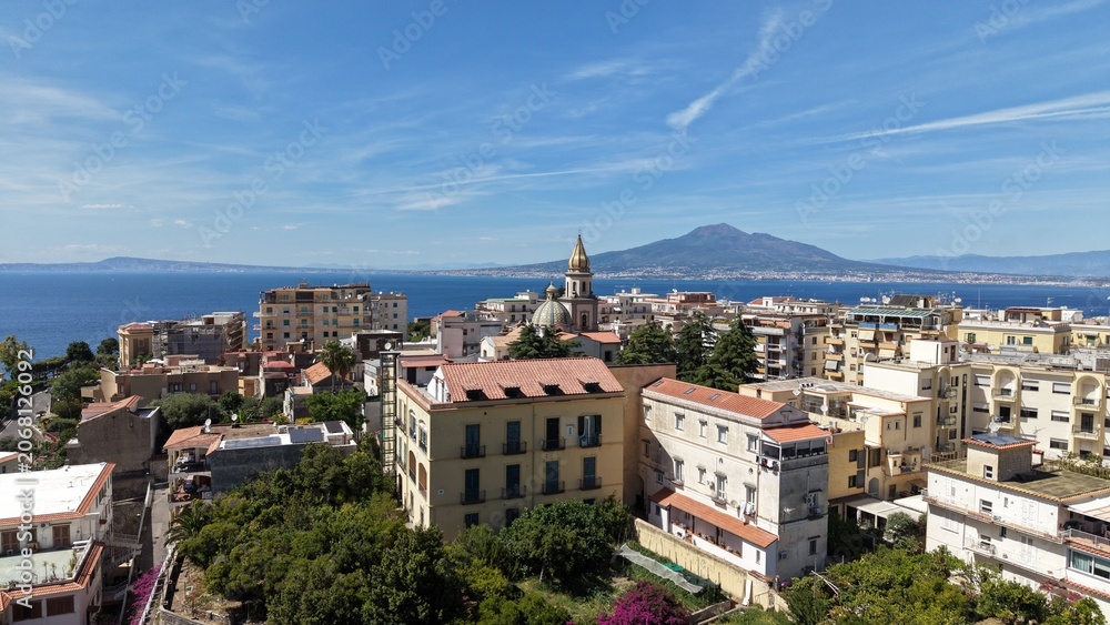 Obraz premium Aerial drone view of Vico Equense town with colorful buildings, church dome and Mount Vesuvius volcano across the Gulf of Naples, Italy 