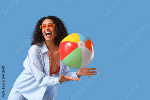 Young African-American woman with beach ball on blue background. Summer party