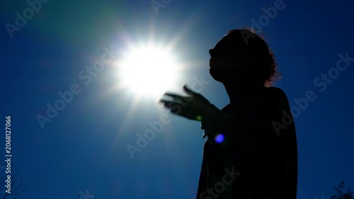 Woman suffers from the heat. A silhouette of a woman against a blue sky and hot sun fans her face with her hands, suffering from the heat.