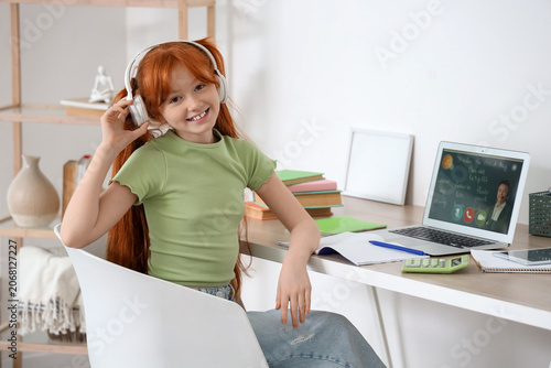 Little redhead girl with laptop studying online at home