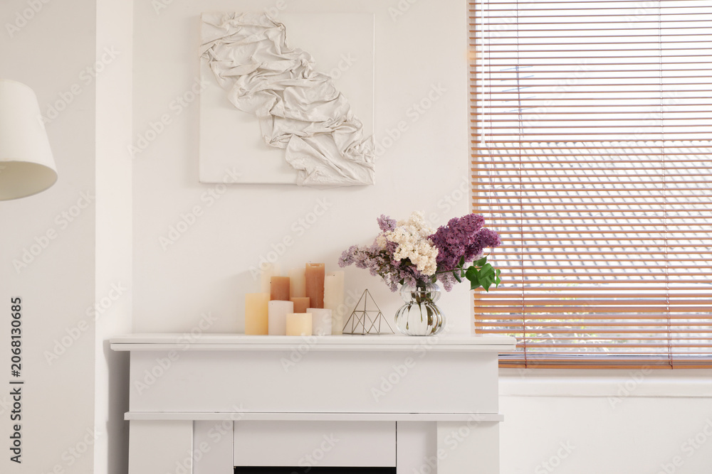 Fototapeta premium Flowers in vase and candles on fireplace in interior of stylish living room