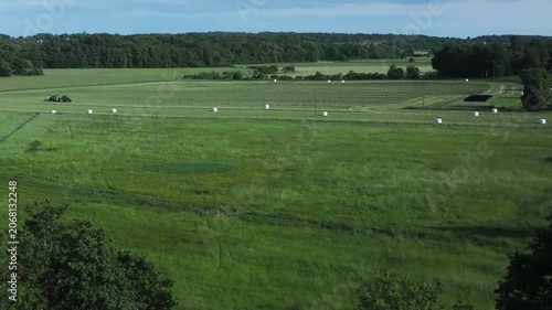 Tractor driving across a large field collecting hay and grass