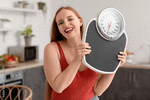 Young overweight woman with scales in kitchen