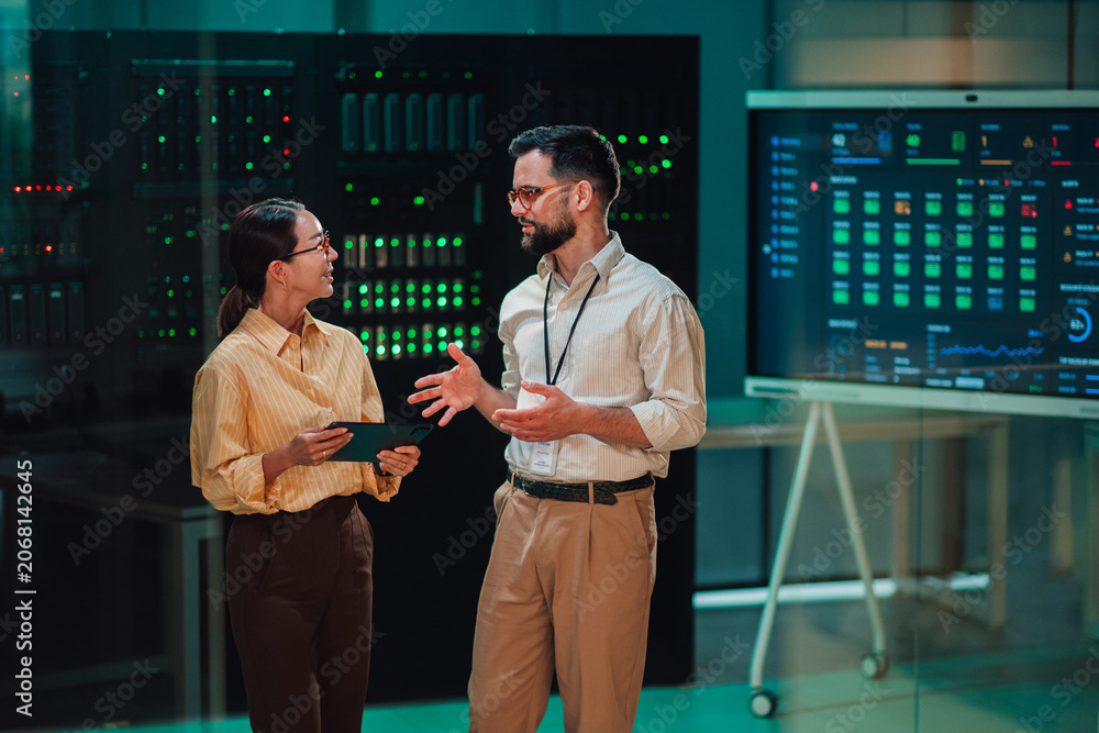 Fototapeta premium It engineers discussing server performance in data center, analyzing information on a dashboard screen