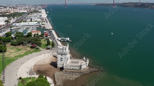 Aerial drone shot of Belem Tower and 25 de Abril suspension bridge over Tagus River in Lisbon. Scenic coastal cityscape with historic architecture and waterfront views