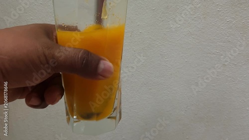 Showing Glass Jar of Orange Juice Being Stirred with Spoon