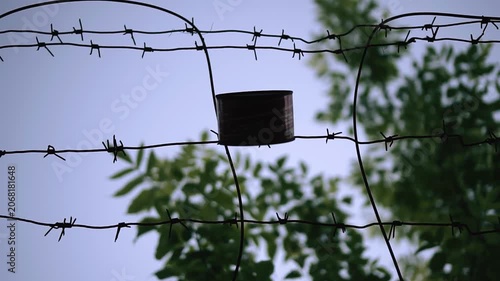 There's a tin can hanging on an old barbed wire fence. Shooting in an abandoned place