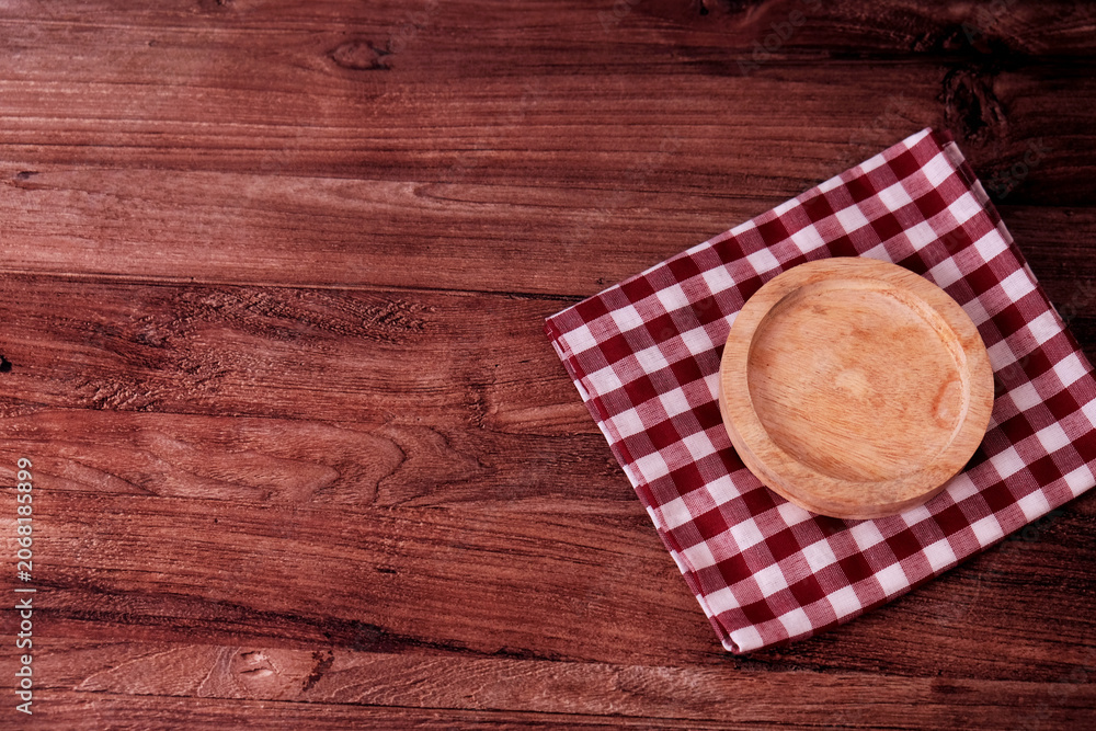 Fototapeta premium Wooden table holds a simple, warm-toned plate. Red and white checkered cloth adds cozy charm. Background features clean, paneled walls. Perfect for cafe, kitchen, or rustic lifestyle scenes