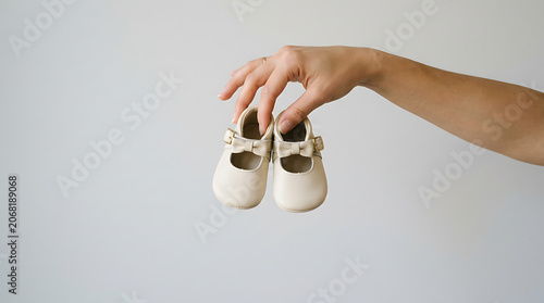 A hand holds baby shoes against a plain background indoors.