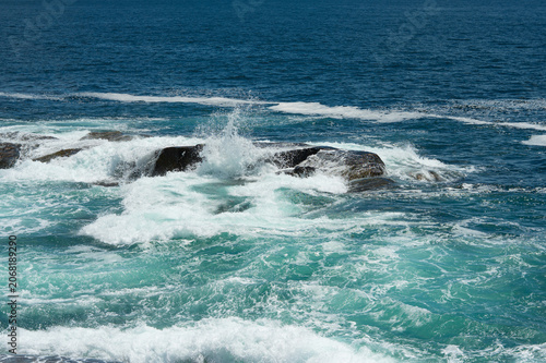 High-energy scene of white sea foam and turquoise ocean waves breaking over granite boulders at Peggy's Cove, Nova Scotia, Canada.