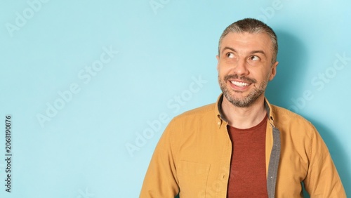 Slika na platnu Smiling Caucasian Man In Mid-age Looking Upward With Joyful Expression In Front Of Solid Blue Background, Capturing Positive Energy And Optimism