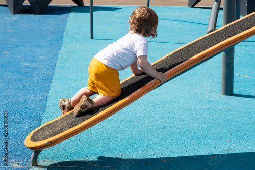 Obraz na plátně Toddler boy climbing up inclined board at playground