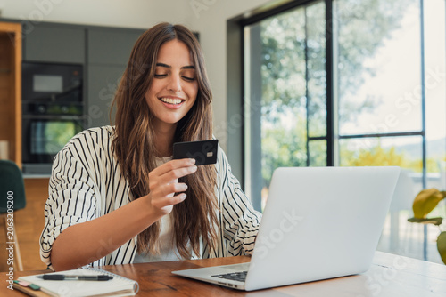 Obraz na plátně Young woman smiling while holding a credit card, confidently making a secure ele