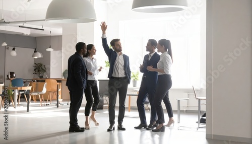 Diverse team collaborating in modern office, one member raising hand in agreement during discussion