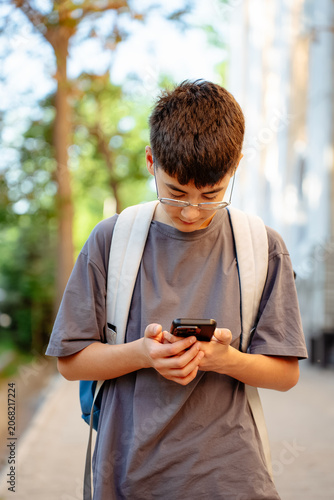 Photography Vertical shot of teen student with backpack uses smartphone outdoors on sunny city street