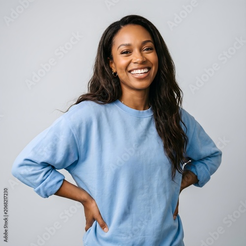 A smiling woman wearing a blue sweatshirt is standing confidently with hands on hips.