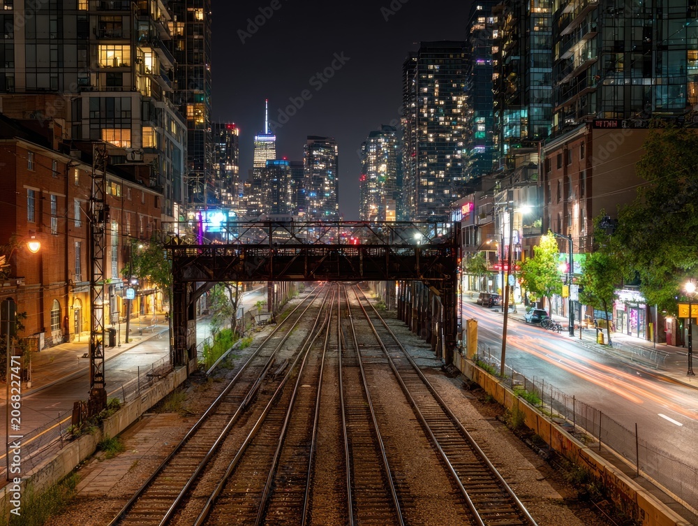 Fototapeta premium City skyline at night with train tracks leading under an overpass