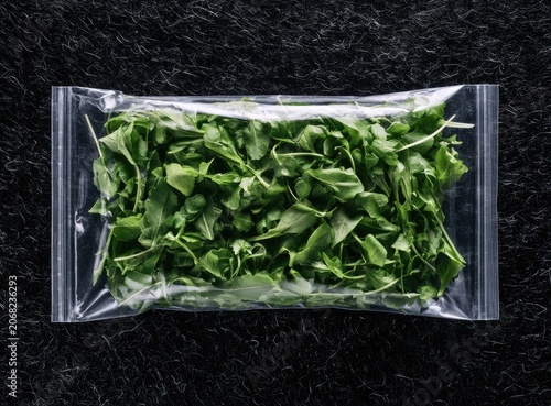 Fresh green leafy vegetables packed in a clear plastic bag on a dark surface