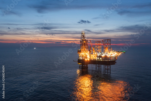 Aerial view from a drone of big jack up offshore drilling oil rig, production platform and supply vessel In the ocean during sunset - Oil and Gas Industry