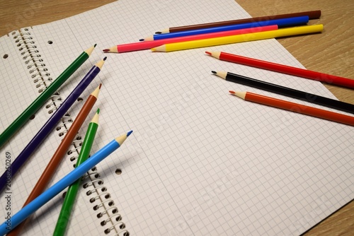 School supplies on a table. Colored pencils scattered on an empty notebook