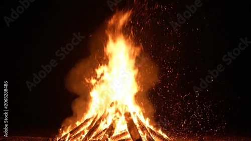 A large bonfire burns brightly with sparks flying in the dark night sky