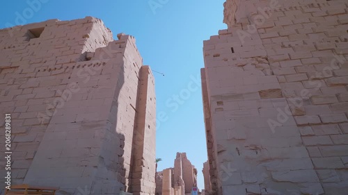 A low angle view showcasing the towering, ancient pylons of the Karnak Temple Complex in Luxor, Egypt, under a clear, vibrant blue sky.