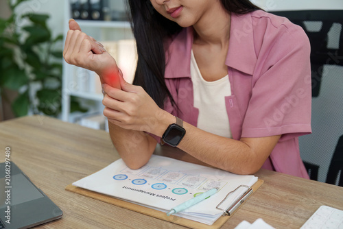 Cropped shot of woman holding painful wrist with red glow over desk for carpal tunnel syndrome