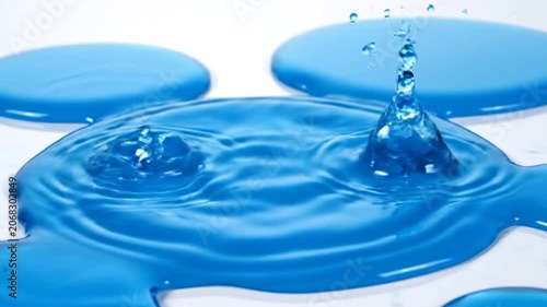 Blue liquid droplets falling onto a clean white surface