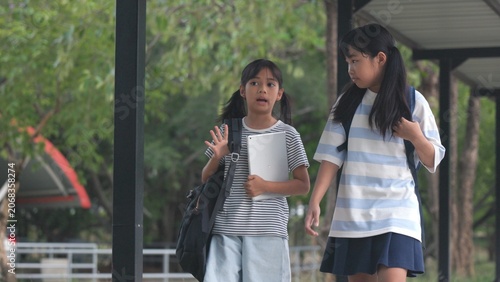 Obraz na plátně Cute Asian girl students carrying heavy backpacks along campus path to build strong friendly classmate relationships