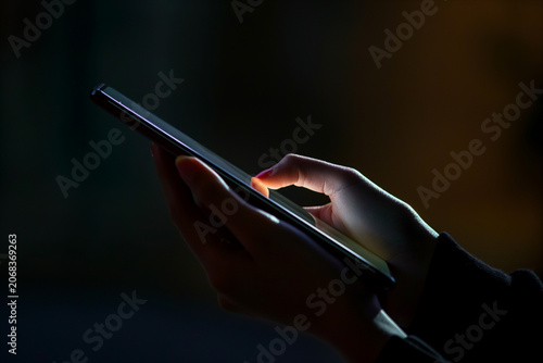 Close-up hands holding phone in darkness with illuminated screen light  