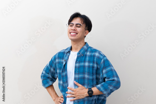 Obraz na płótnie A satisfied young Asian man smiling and rubbing his stomach after a delicious meal against a plain studio background