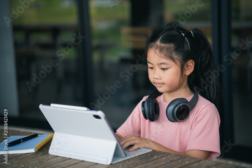 Young Girl Concentrating on Digital Tablet at Table with Headphones in Modern Indoor Space with Large Windows and Natural Light, Educational and Technology Focus