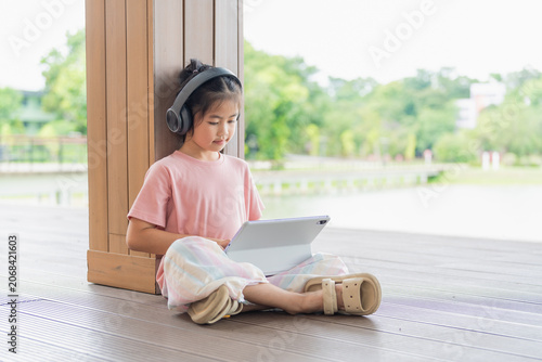 Young Girl Using Tablet Device While Sitting on Wooden Floor Near Large Window in Bright Indoor Space with Green Nature Outside