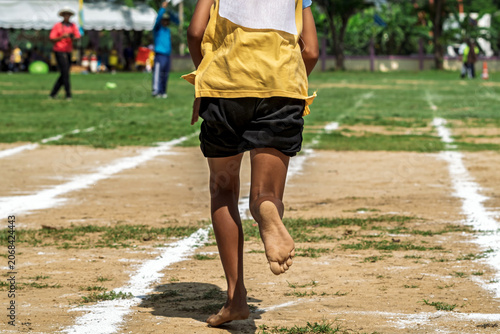 Schoolgirls sprinting toward finish line at sports day. Back view of young schoolgirls competing in running race on grass and dirt field track, sprinting towards finish line during school sports day