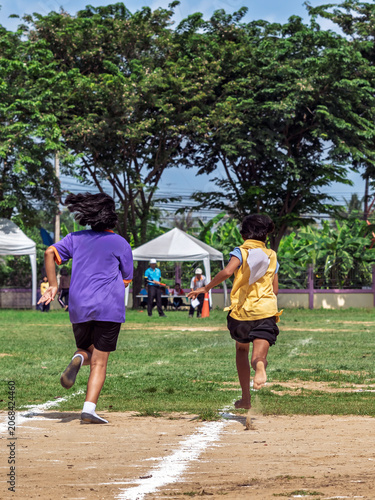 Schoolgirls sprinting toward finish line at sports day. Back view of young schoolgirls competing in running race on grass and dirt field track, sprinting towards finish line during school sports day