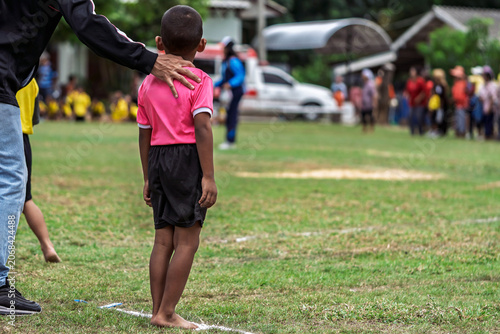 Teacher or coach supporting young boy student at school sports day. Male teacher or coach putting his hand on young schoolboys shoulder to encourage and support him while standing barefoot on field.