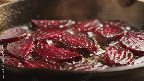 Sliced red beets searing in hot oil in a cast iron pan, featuring caramelized edges, rising steam, and bubbling liquid during the pan-frying process in a kitchen setting.