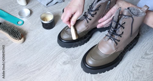 Polishing leather winter boots with wax brush in bright minimalist room. Shoes care routine concept features close up hands applying organic cream on stylish footwear surface. Household domestic