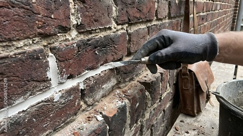 Professional brick repointing process, mason hand in black glove applying white mortar to old red brick wall, masonry restoration and building maintenance