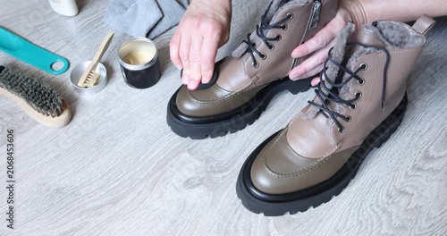 Applying natural wax on leather boots with round sponge inside bright room. Footwear care routine concept features close up human hands restoring stylish autumn shoes surface. Household domestic