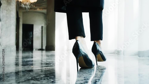 Elegant woman in high heels walks gracefully across a polished marble floor, showcasing stylish footwear and a sophisticated setting with bright natural light