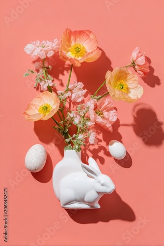 Easter floral arrangement in rabbit vase with spring poppies and white eggs on peach background, flat lay composition for seasonal holiday marketing and copy space
