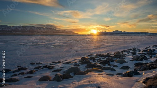 Winter sunset over frozen lake with snowy shore and mountains