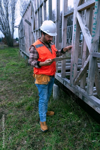 Construction supervisor inspecting wood framing on-site using a digital tablet