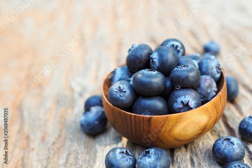 Fresh blueberries in a small wooden bowl on rustic wooden background with copy space.